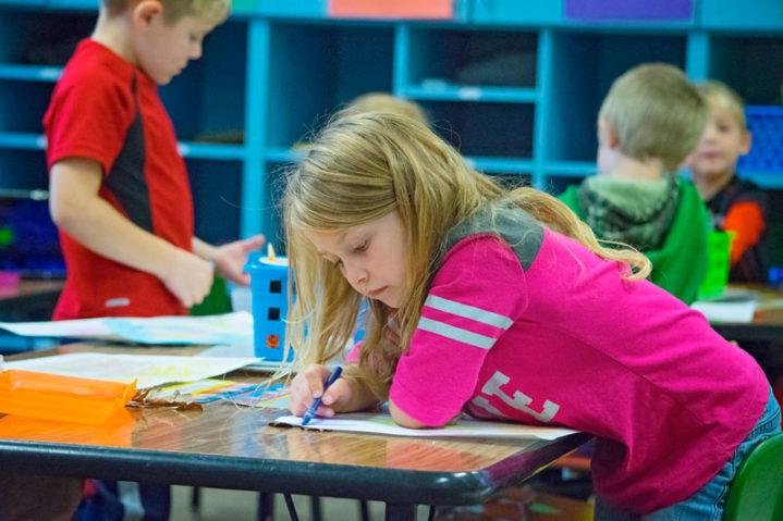 Girl Coloring with blue crayon in classroom