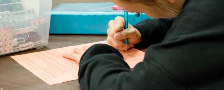 Female student writing on coral paper with pencil